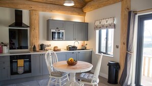 A modern kitchen with grey cabinets, a built-in oven, and a dining area with a round table and two chairs. - Braisty Woods - Hopes & Beams (Harrogate)