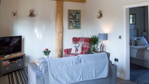 A living room with a television, a sofa, a plaid chair, and a decorative wall piece. - Braisty Woods - Hopes & Beams (Harrogate)