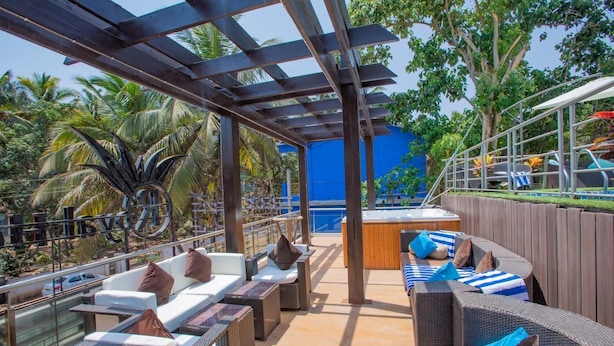 An outdoor lounge area with wicker furniture, a pool, and a view of palm trees. - Nitya Resort (Calangute)
