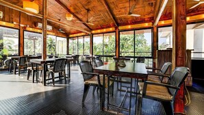 A spacious indoor dining area with wooden ceiling beams, large windows, and a variety of seating arrangements. - Nitya Resort (Calangute)