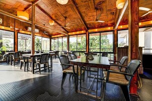 A spacious indoor dining area with wooden ceiling beams, large windows, and a variety of seating arrangements.