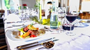 Une table à manger dressée avec des assiettes remplies de nourriture, des verres à vin et des couverts.