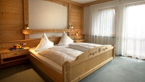 Un lit à baldaquin en bois, agrémenté de draps blancs, une table de chevet avec un panier de fruits et un grand miroir au-dessus du lit.