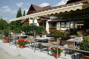 An outdoor café with tables and chairs, surrounded by potted plants and a building with a tiled roof. - Landgasthof Löwen (Neubulach)