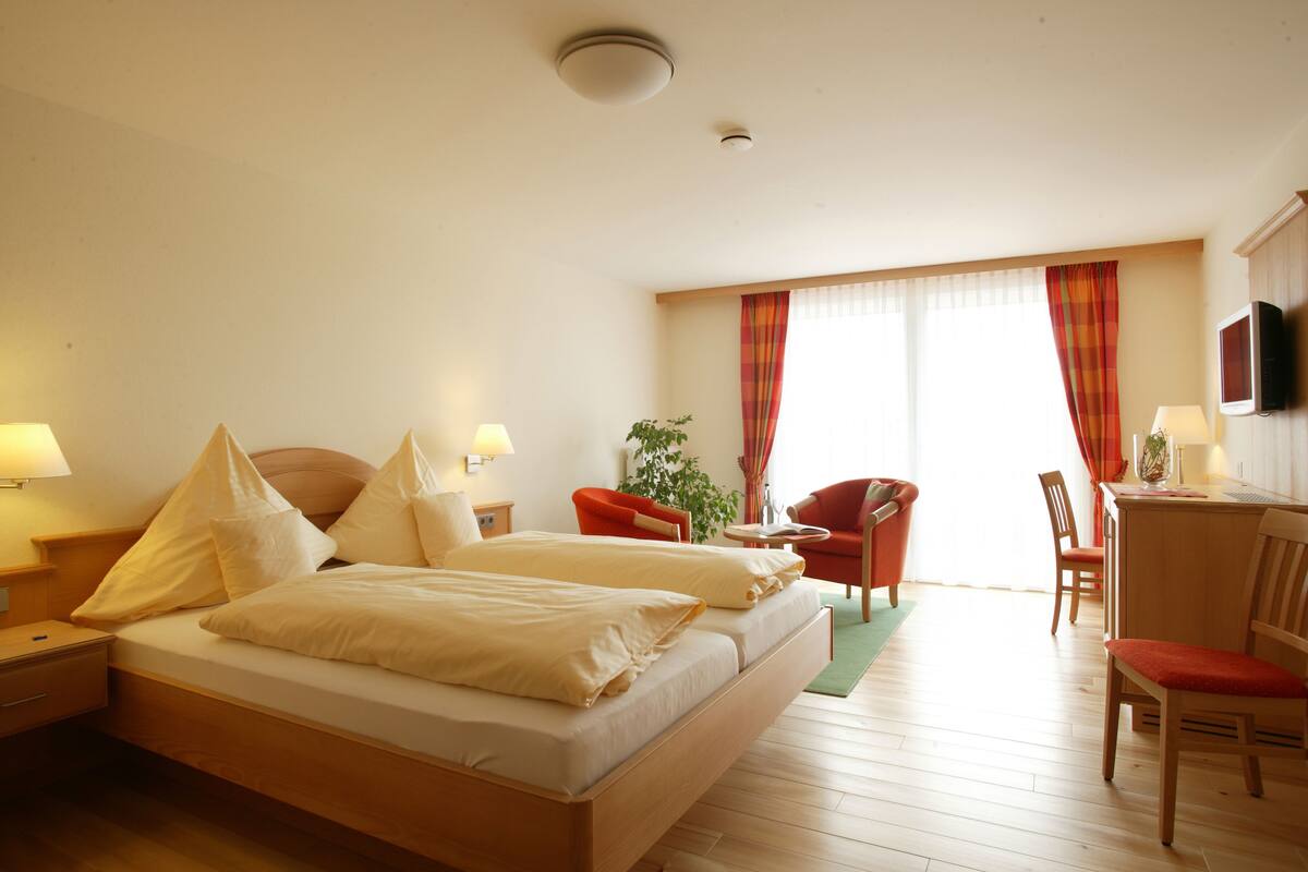 Habitació d'hotel amb un llit doble, dues taules de nit amb làmpades, escriptori amb cadira, televisió i finestra amb cortines.