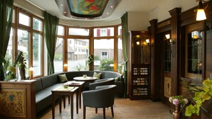 Une pièce accueillante avec un plafond voûté, de grandes fenêtres, un comptoir d’accueil en bois et un coin salon avec un canapé et des fauteuils.