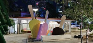 A public space with a colorful sculpture and a building with illuminated signage in the background. - CASA GLORIA (Santiago de Cuba)