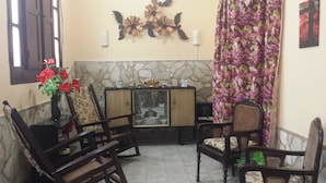 A corner room with a stone wall, a wooden cabinet with glass doors, a floral curtain, and a wooden chair with a cushion. - CASA GLORIA (Santiago de Cuba)