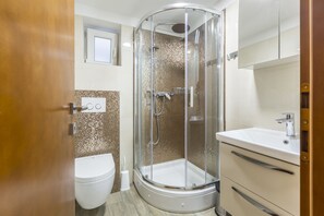Uma casa de banho moderna com chuveiro envidraçado, sanita e lavatório com espelho em cima.