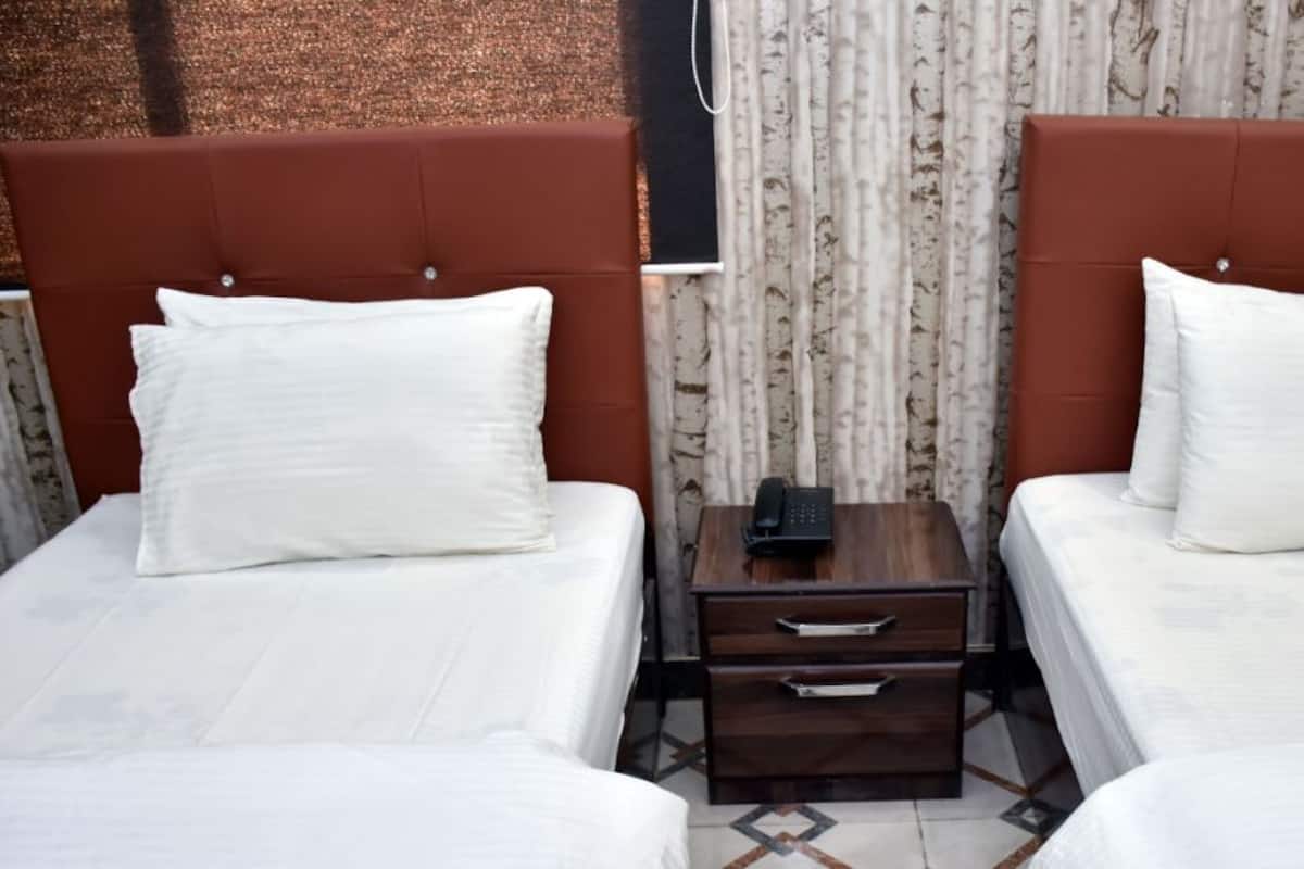 A hotel room with two beds, each with white bedding and a brown headboard. There is a small wooden nightstand between the beds with a telephone and a drawer.