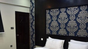 A hotel room with a large bed, dark headboard with a patterned design, and a door to the left.