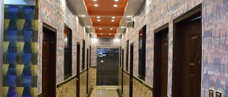 A hotel corridor with a polished floor, patterned walls, and a ceiling with recessed lighting.