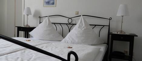 Un lit bien fait, avec du linge de lit blanc, deux tables de chevet avec des lampes et un tableau encadré au mur.