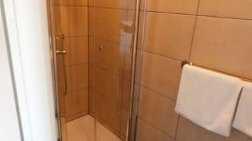 Eine Dusche mit Glastür, ein weißes Handtuch an der Wand und ein Fliesenboden.