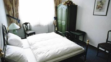 Een net opgemaakt bed in een kamer met een groene garderobe, een stoel en een lamp.