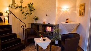 A cozy living room with a fireplace, a staircase, and a small table with a vase. - Hotel Restaurant Jägerhof (Mayen)