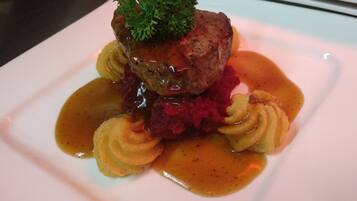 Un plato con un guiso de carne como pieza central, adornado con perejil, rodeado de un puré rojo y una salsa marrón.