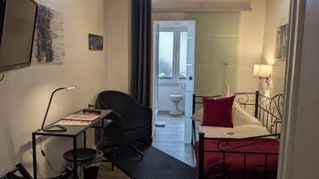 Habitación de hotel compacta con escritorio, silla y cama con almohada roja.
