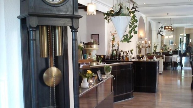 A grand clock, a wooden reception desk, and a spacious bar area with a high ceiling and modern lighting. - Hotel Restaurant Jägerhof (Mayen)