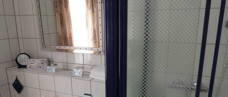Baño con lavamanos, espejo, ducha y perchero para toallas.