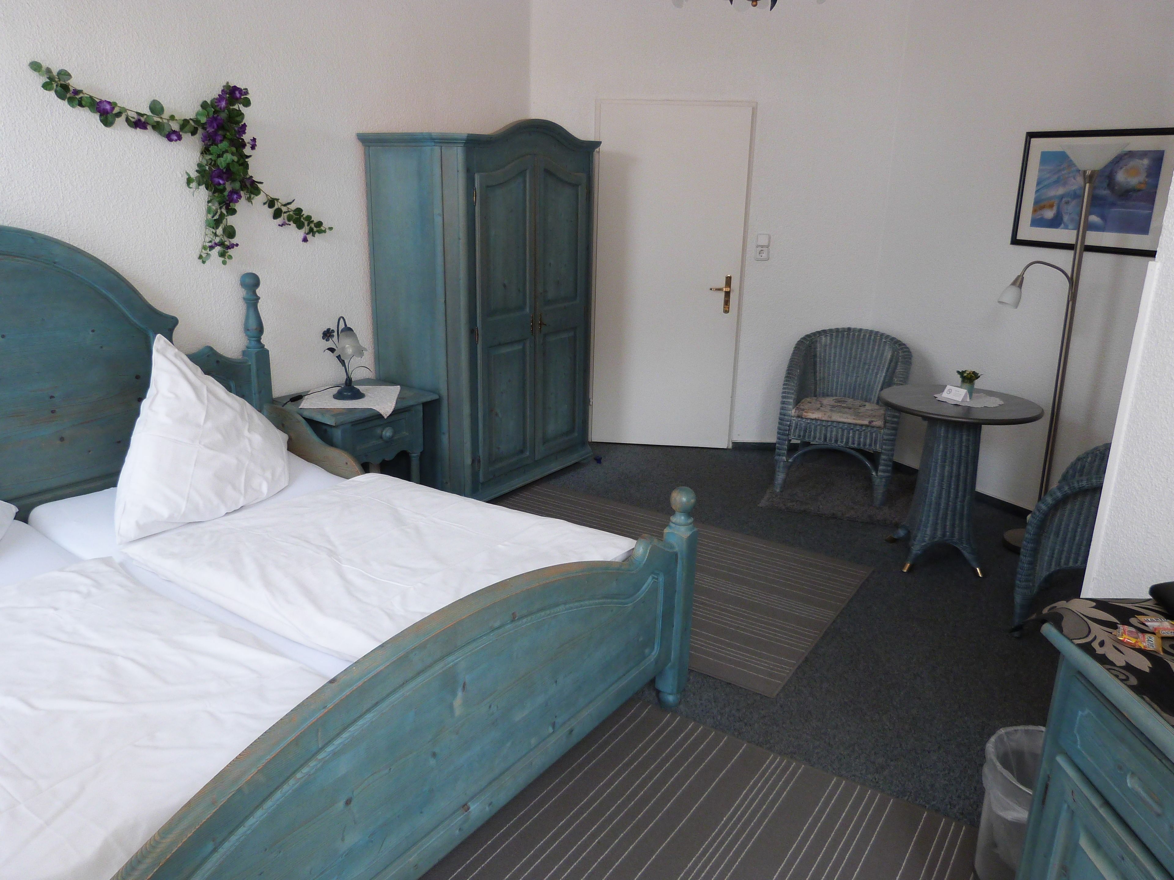 A bedroom with a bed, a wardrobe, a chair, a small table, and a picture on the wall.
