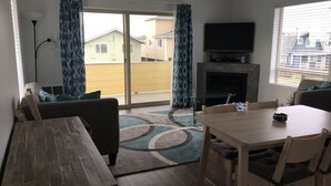 Een woonkamer met een houten tafel en stoelen, een bank, een glazen salontafel, een open haard en een tv aan de muur.