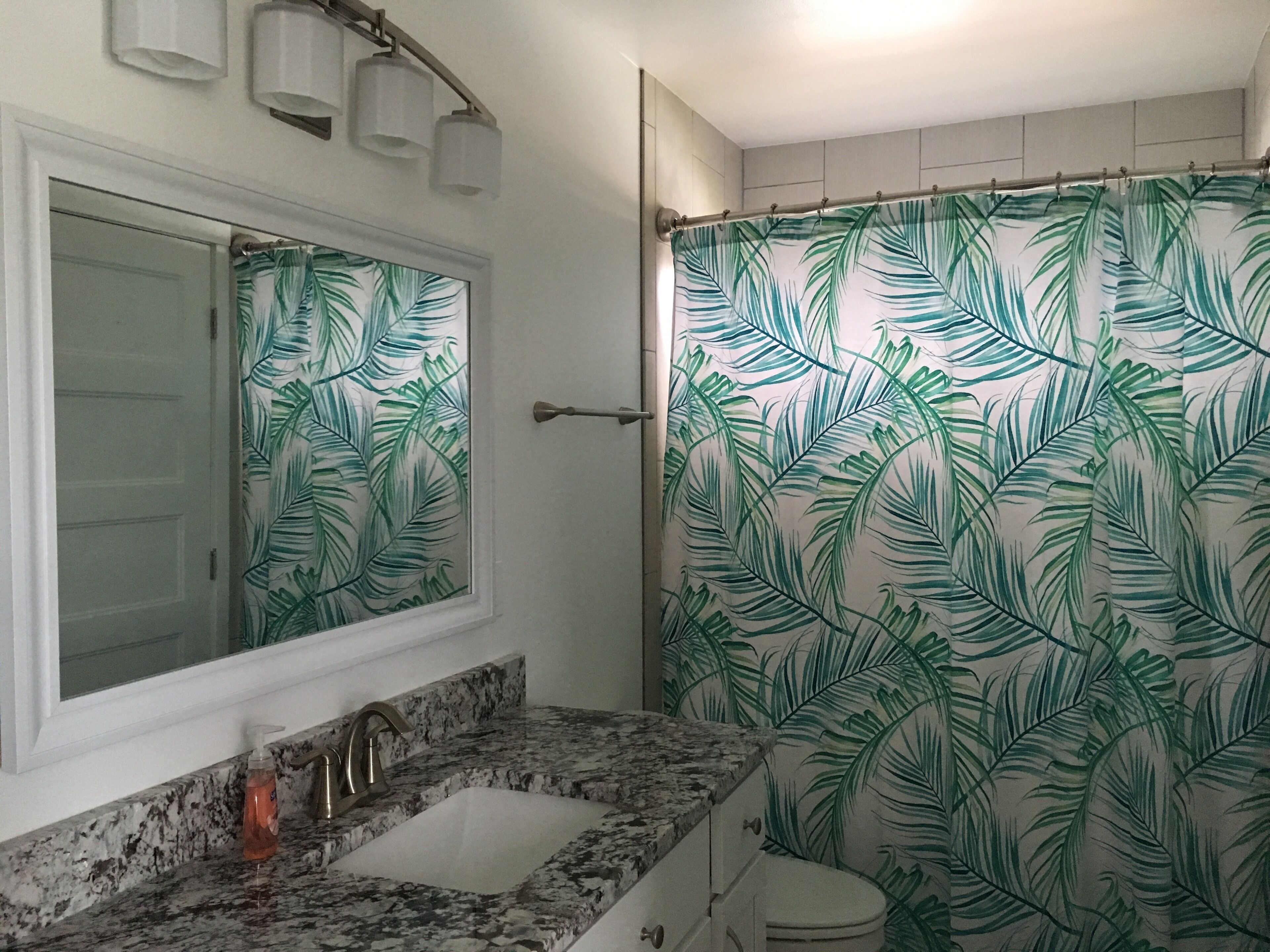A bathroom with a sink, mirror, and shower curtain with a leaf pattern.