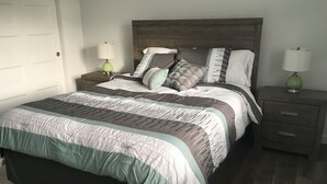 Een netjes opgemaakt bed met een gestreept dekbedovertrek, twee nachtkastjes met lampen, en een houten hoofdbord.