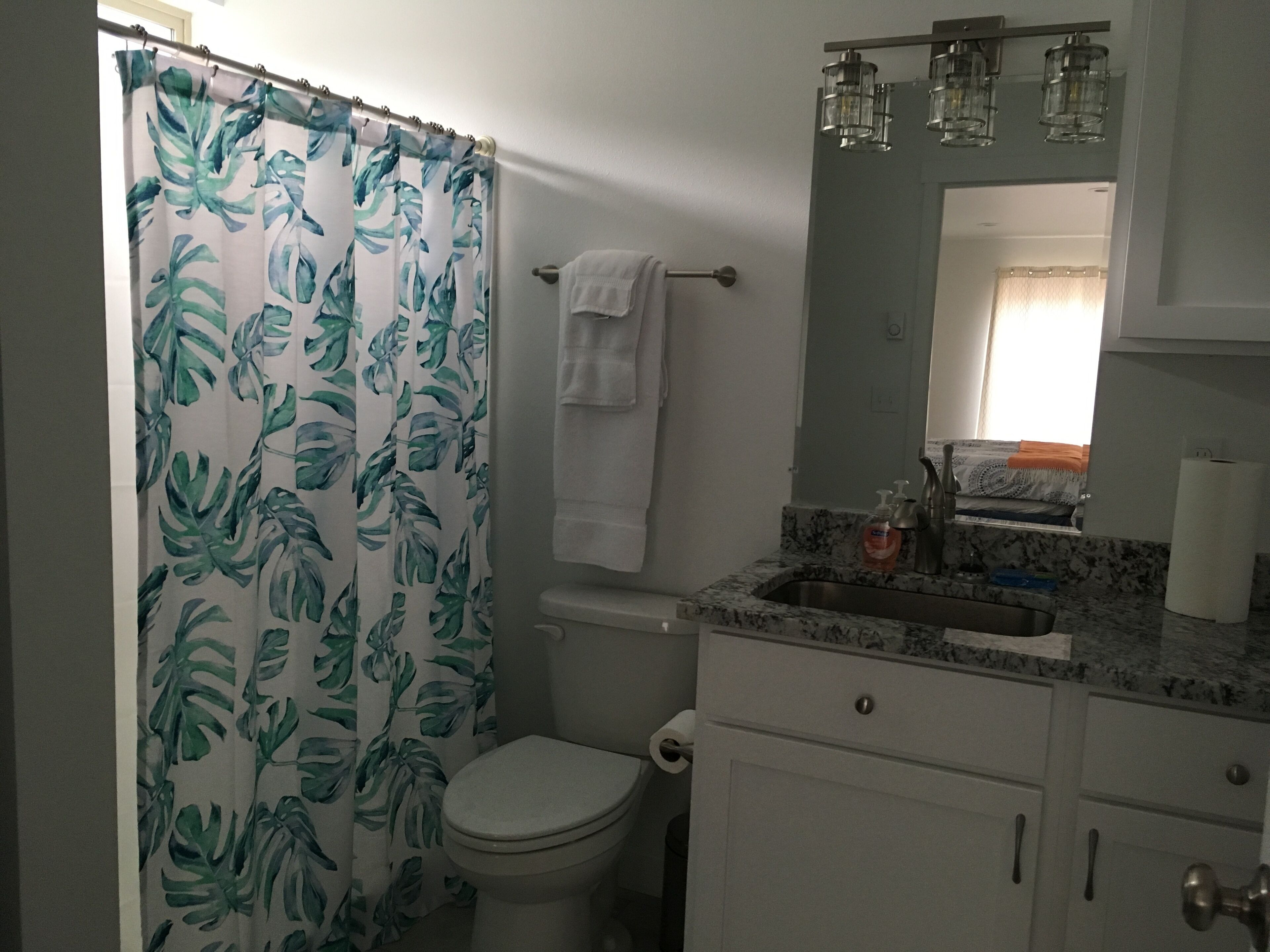 A bathroom with a toilet, sink, and shower curtain with a leaf pattern.