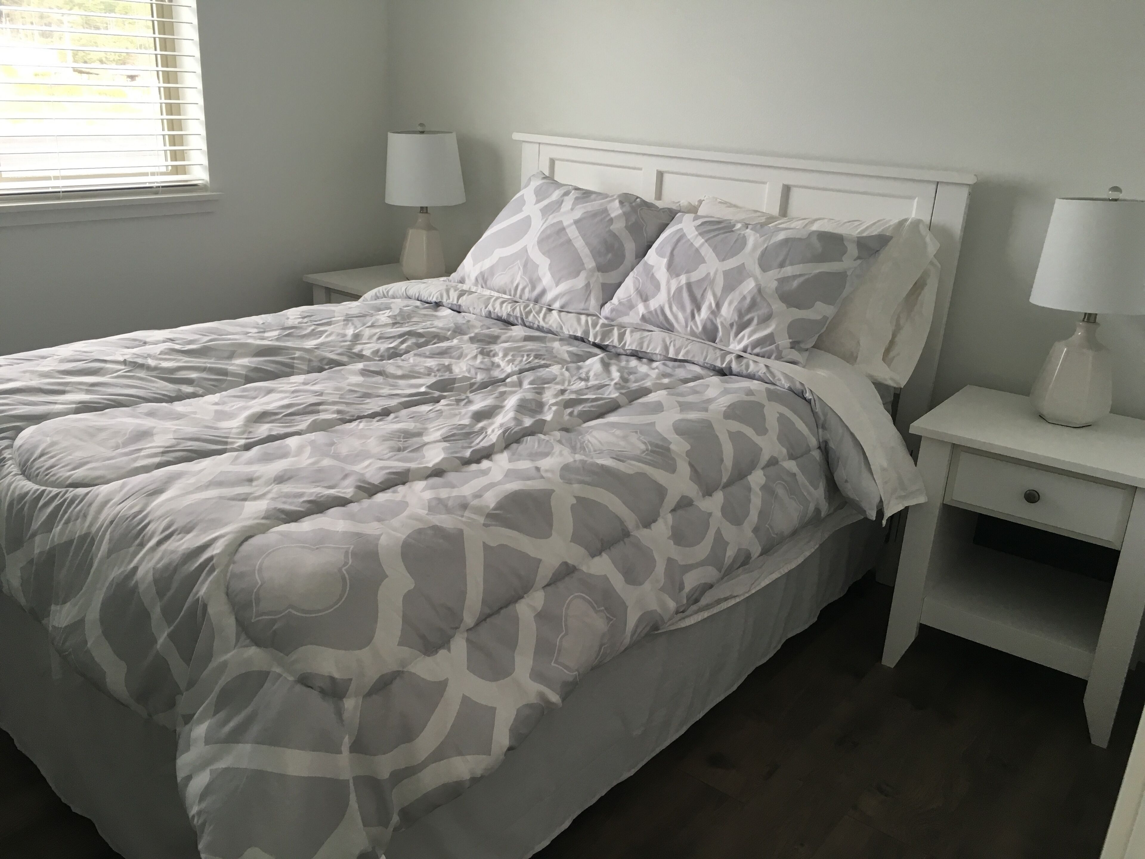 A neatly made bed with a patterned bedspread, two bedside tables with lamps, and a window with blinds.