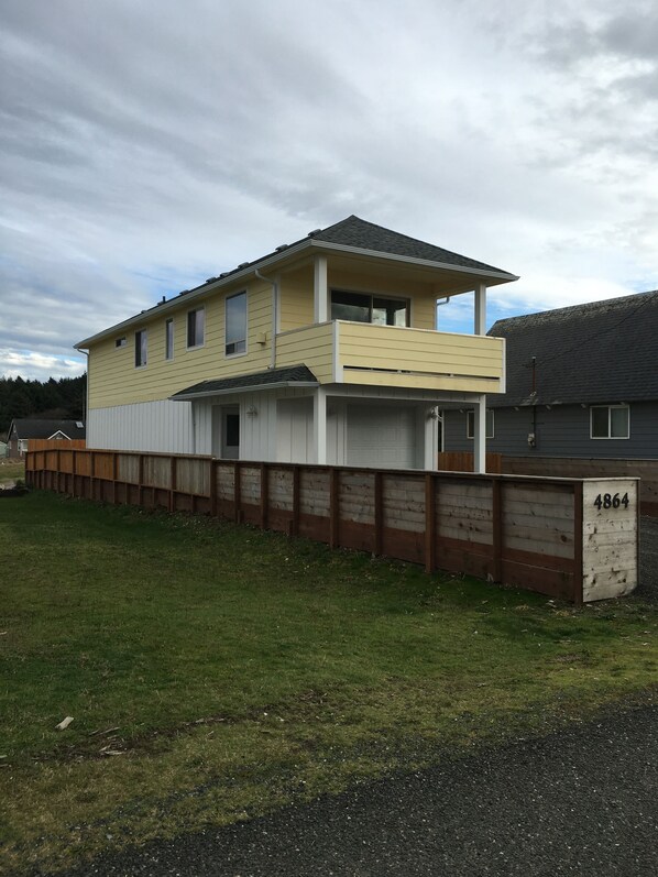 A two-story house with a balcony, a fenced yard, and a number '4864' sign. - Reel Bliss Beach House (Moclips)