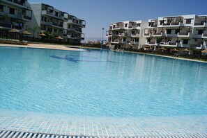 A swimming pool with tiled edges, surrounded by multi-story buildings with balconies and outdoor seating areas. - Résidence Mirador Golf Cabo Negro (M'diq)