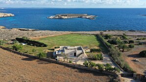 A coastal property with a large grassy area, a modern house with a flat roof, and a view of the sea and rocky outcrops. - Villa Pirreca (Favignana)