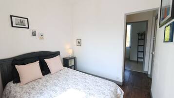 A bedroom with a bed, bedside table, and a nightstand. There are framed pictures on the wall.