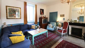 Un salon avec un canapé bleu, une table basse en bois, un tapis rouge à motifs, un fauteuil bleu et une cheminée.
