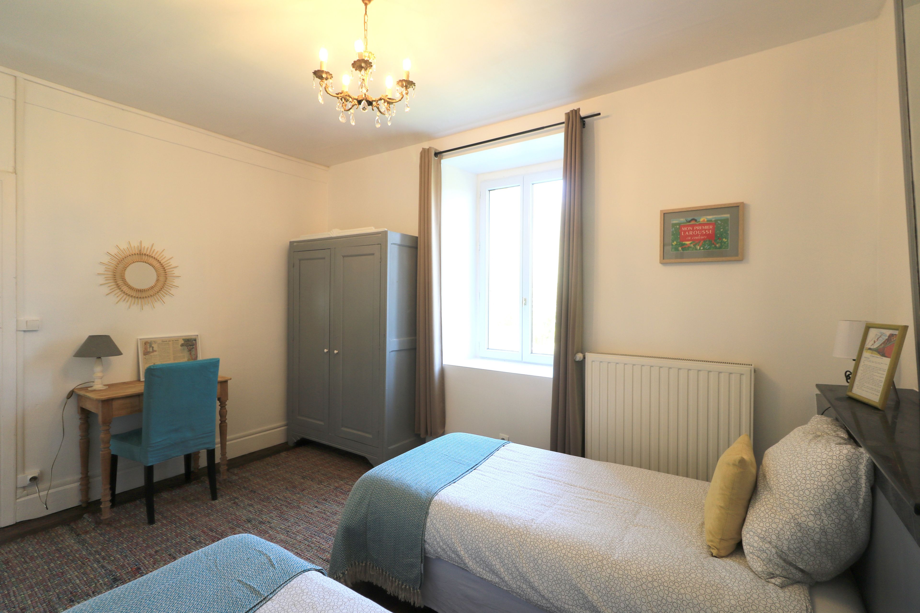A bedroom with two single beds, a desk with a chair, a wardrobe, and a window with curtains.