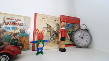 Una estantería con libros, un coche de juguete, una figurita de madera y un reloj.