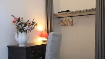 A small, neatly arranged bedroom with a desk, chair, and a bedside table with a lamp.