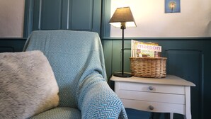 Une pièce avec un fauteuil à motifs, une petite table de chevet avec une lampe, un panier et un livre intitulé « maison » accroché au mur.