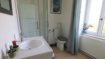 A bathroom with a sink, toilet, shower, and a poster on the wall.