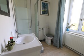 Une salle de bain avec un lavabo, des toilettes, une douche et une affiche accrochée au mur.