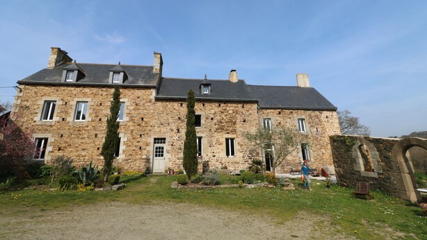 Un bâtiment en pierre doté de nombreuses fenêtres et d’un jardin à l’avant.