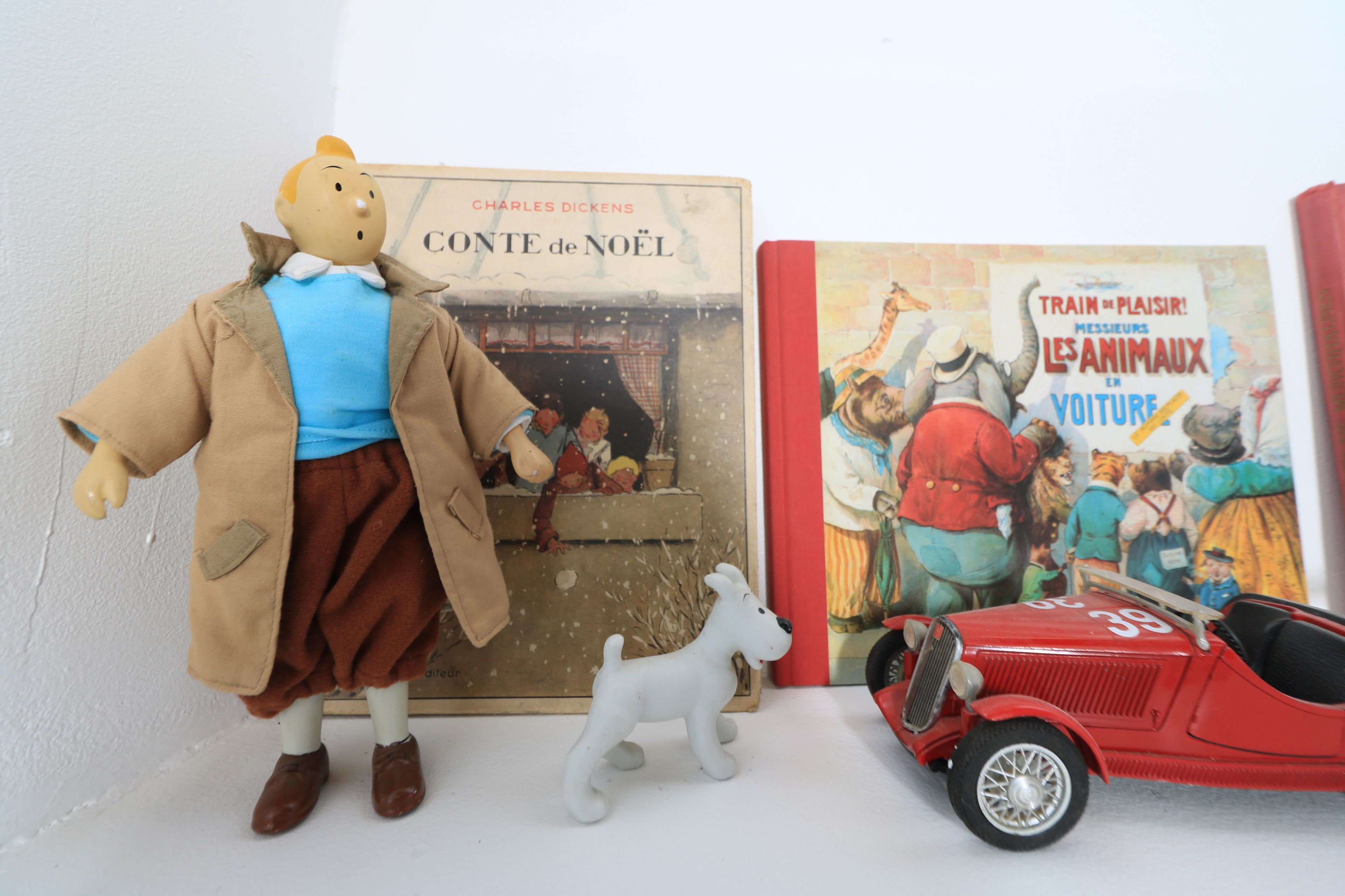 Ein Regal mit einem Buch mit dem Titel 'Conte de Noël' von Charles Dickens, einem Spielzeughund und einem Spielzeugauto.