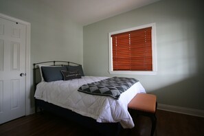 A bedroom with a bed, a bench, a window with blinds, and a door.