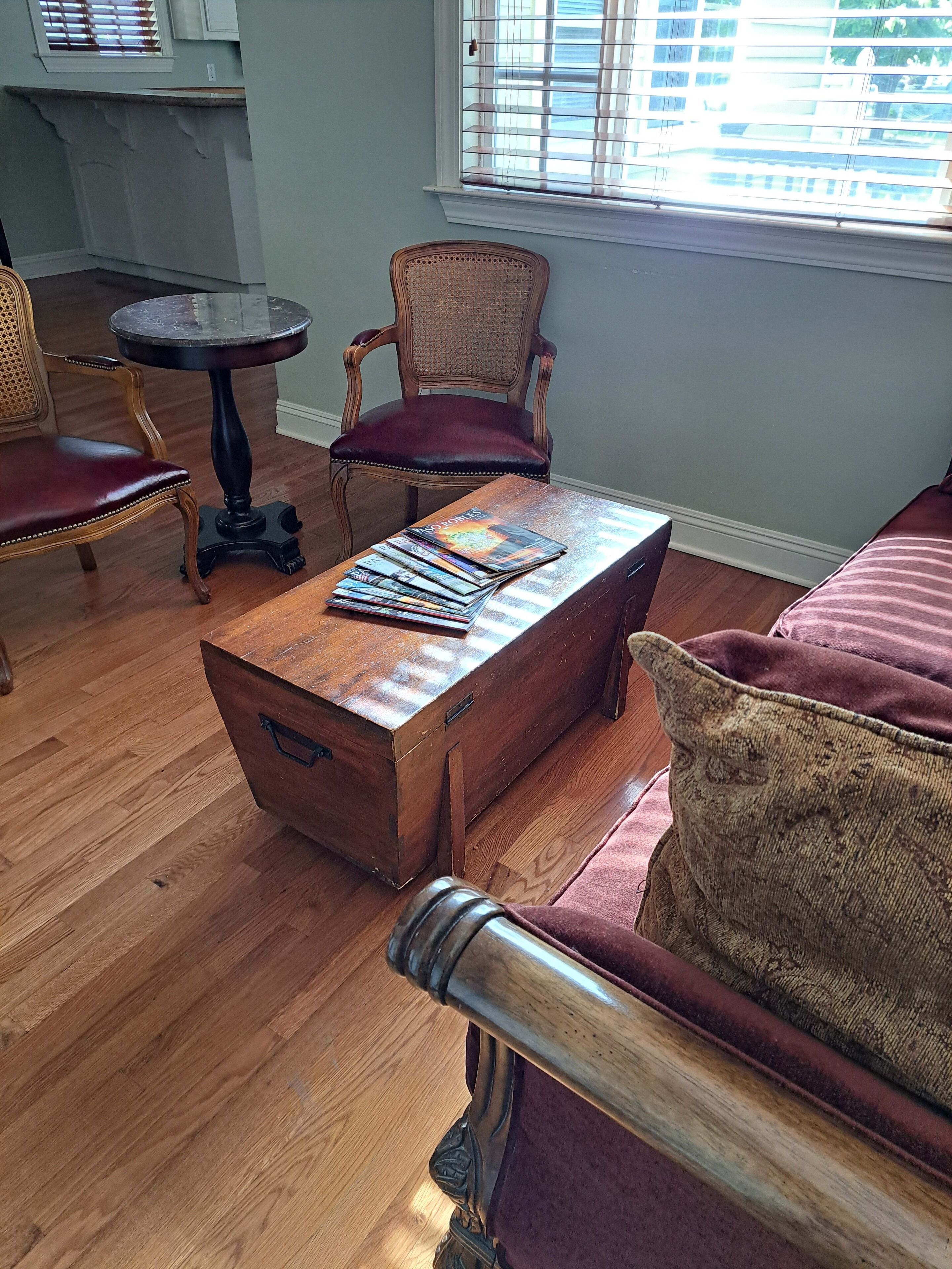 A room with a wooden coffee table, a wicker chair, a cushioned sofa, and a window with blinds.