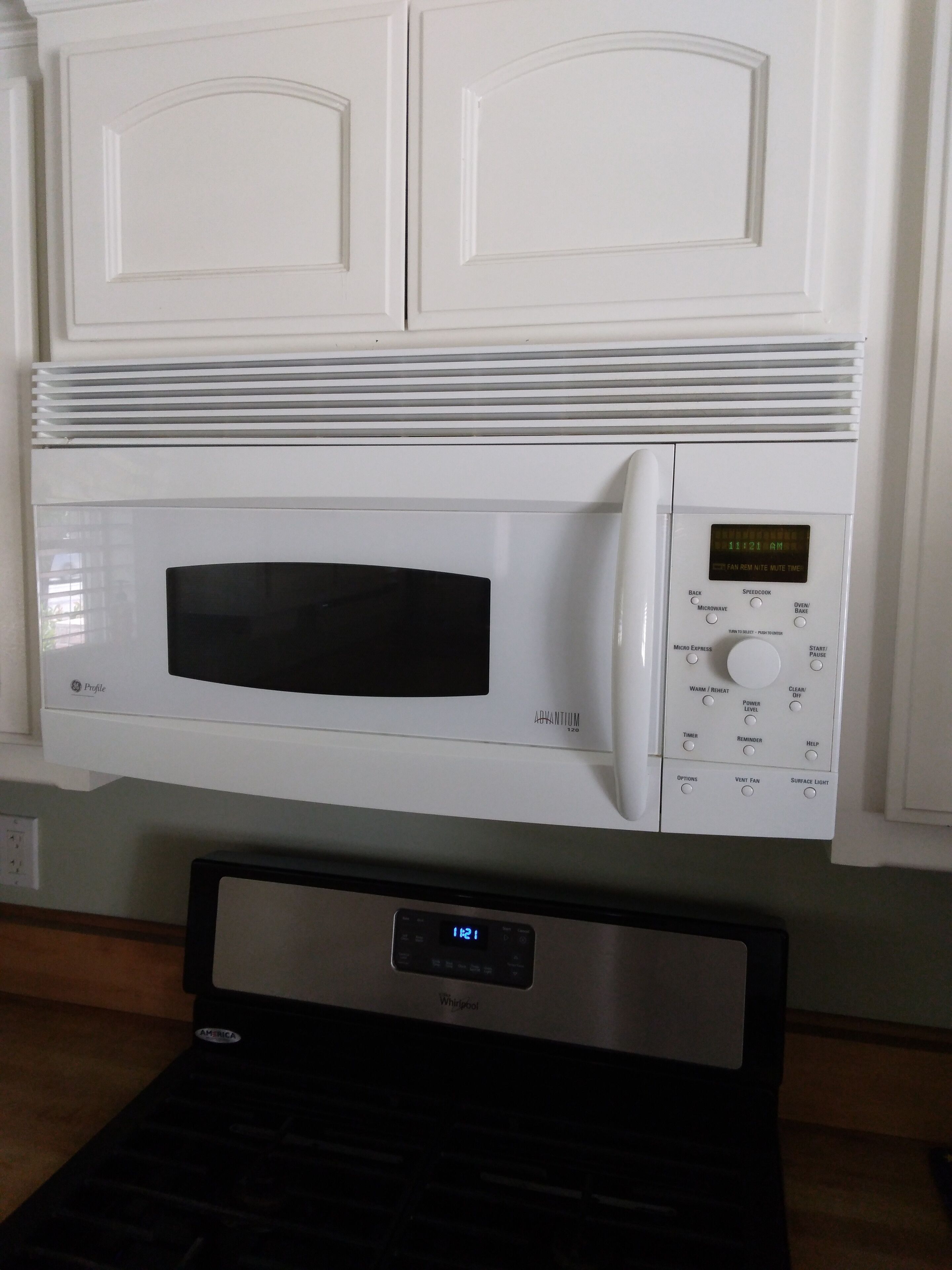 Un four à micro-ondes blanc, doté d’un écran numérique et d’un panneau de commande, fixé au mur au-dessus d’un plan de travail noir.