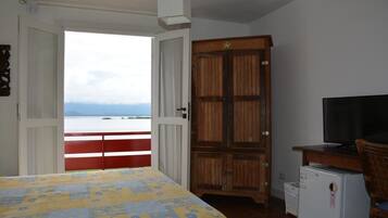A bedroom with a bed, a television, a wardrobe, and a view of the sea.
