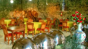 Un restaurante con mesas y sillas de madera, un jarrón decorativo con flores y un muro de piedra de fondo.