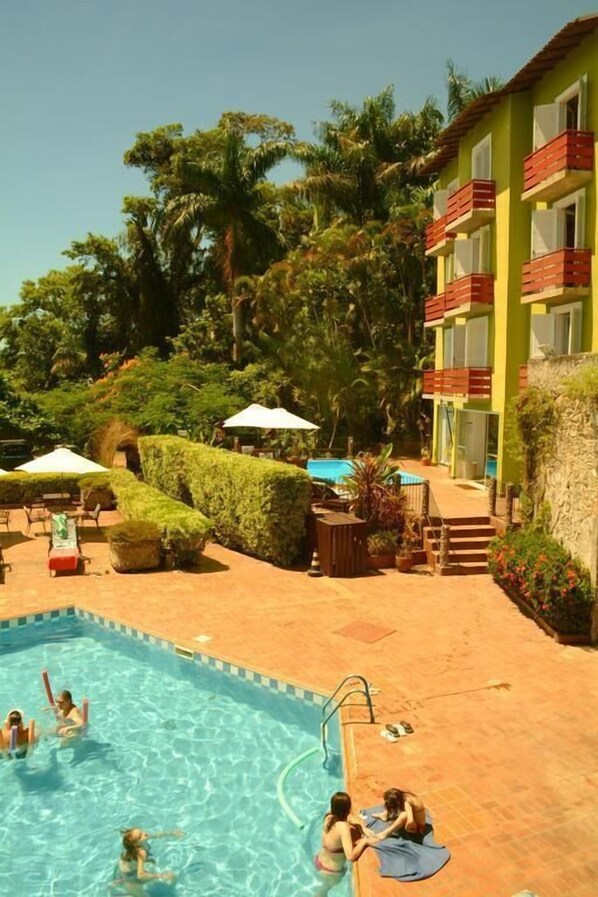 A swimming pool area with a pool, lounge chairs, and a building with balconies. - Camboa Capela Hotel (Antonina)