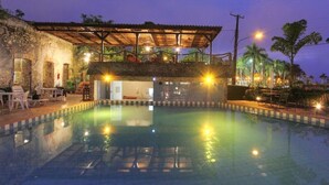 Una piscina con una zona de estar cubierta, un edificio de piedra y vistas del paisaje circundante.